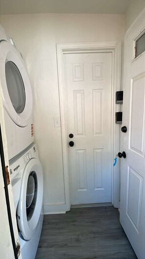 Een wasserette met een witte deur, een wasmachine en een droger die boven elkaar staan.