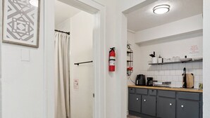 Et moderne køkken med grå skabe, trægulv og en brandslukker monteret på væggen.