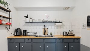 Et køkken med lysegrå skabe, en træbordplade, en kaffemaskine, en brødrister og en vask.