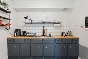 Een keuken met grijze kastjes, een houten aanrecht, een koffiezetapparaat, een broodrooster en een spoelbak.