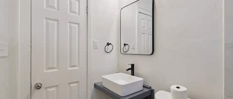 A bathroom with a white door, a white sink, a mirror, and a toilet paper holder.