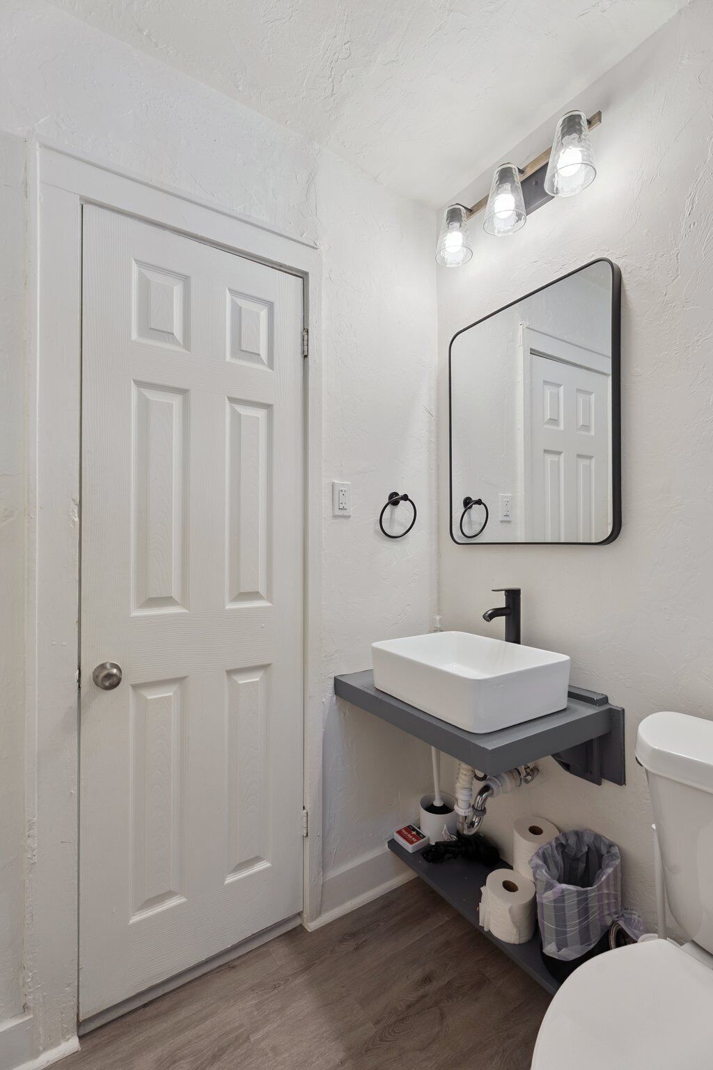 Un bagno con una porta bianca, un lavandino bianco, uno specchio e un water.