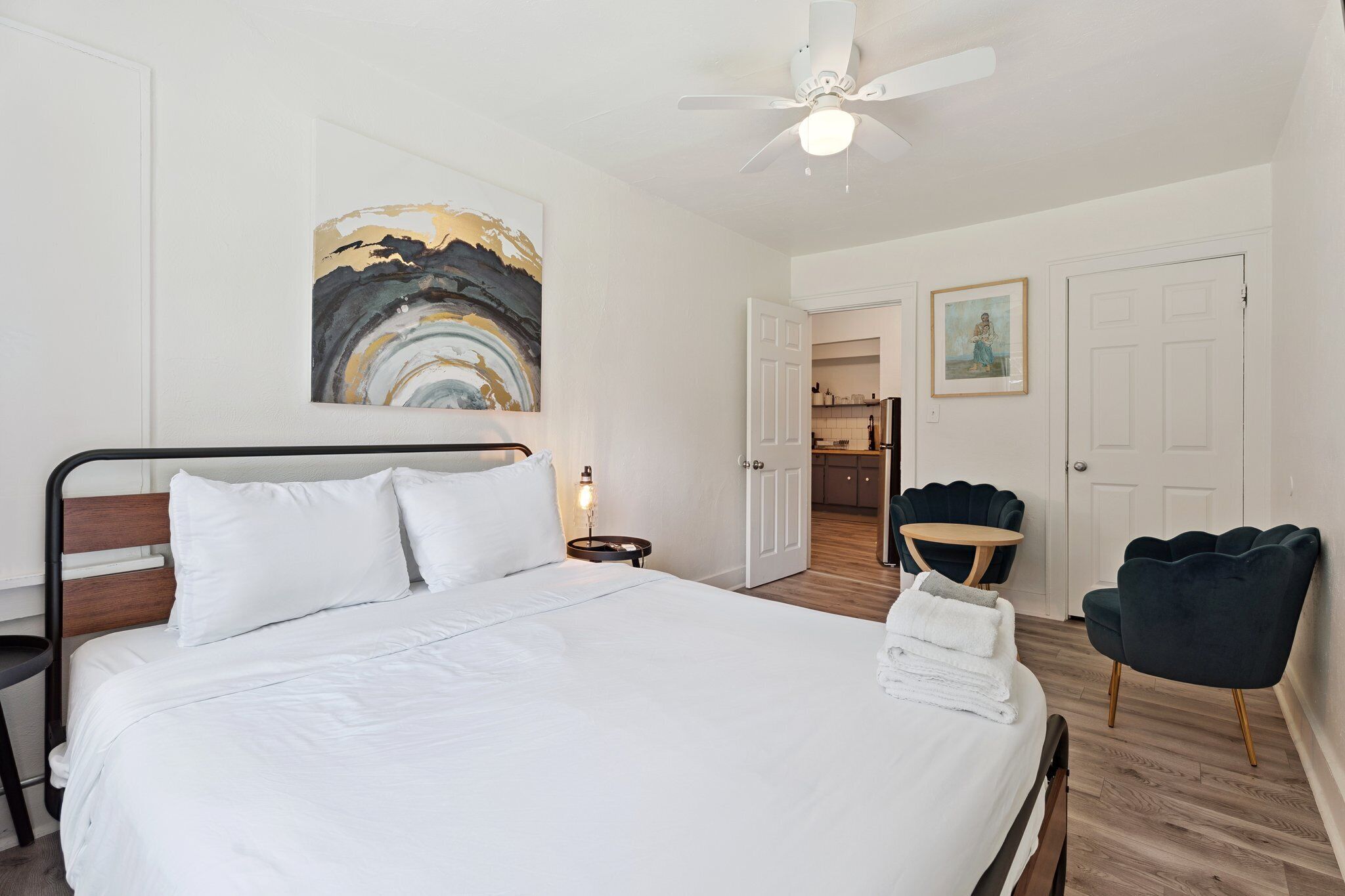 A neatly made bed with white linens, a ceiling fan, and artwork on the wall.