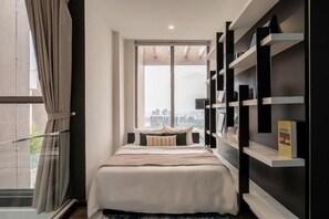 Un dormitorio moderno con cama, ventana grande y estantería empotrada.