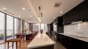 A modern kitchen with a marble island, black cabinets, and a dining area with red chairs. - Stunning Penthouse in the City Centre (Ho Chi Minh City)