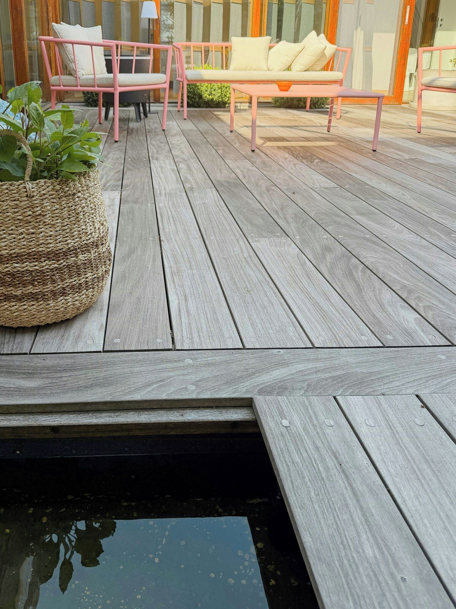 Terraza de madera con dos sillas rosas y una cesta tejida.
