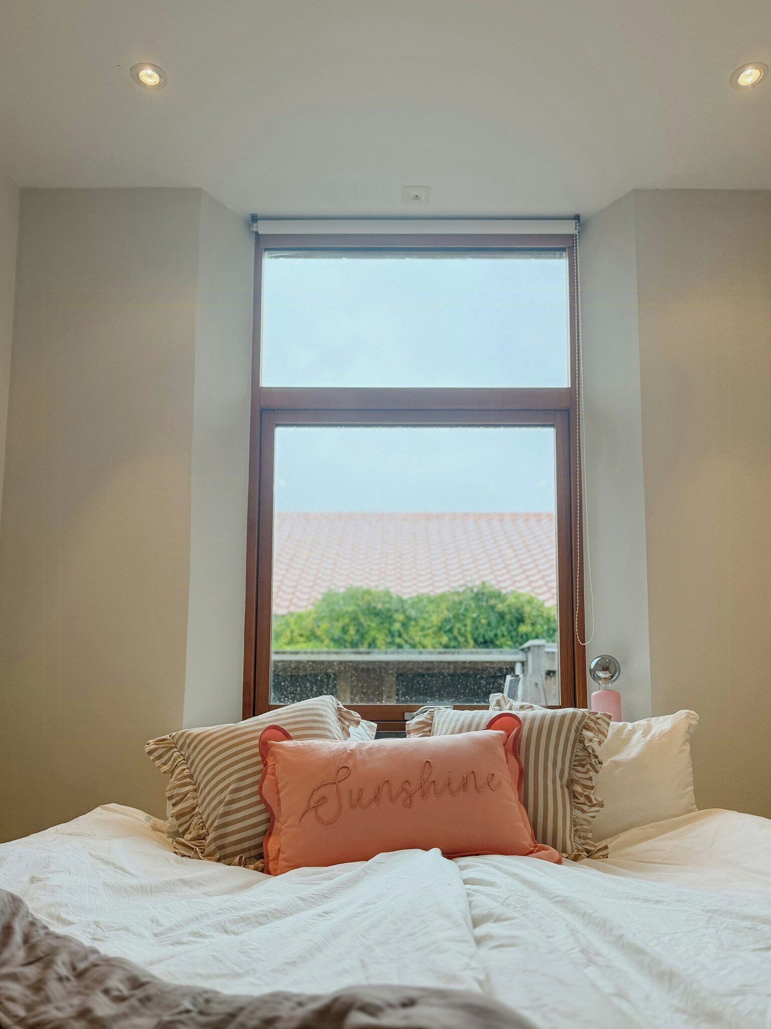 A bedroom with a large window, a bed with striped pillows, and a view of greenery and a building.