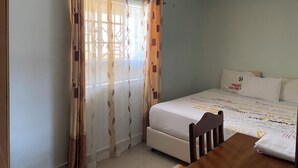 A bedroom with a bed, a wooden chair, a table, and a window with curtains. - Place to stay in Nairobi (Nairobi)