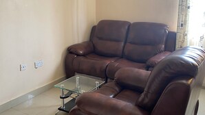 A living room with a brown leather sofa, a glass coffee table, and a tiled floor. - Place to stay in Nairobi (Nairobi)