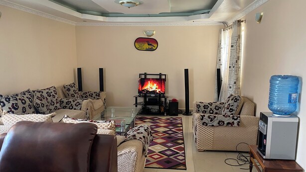A living room with sofas, a glass coffee table, a fireplace with a fire, a water dispenser, and a television. - Place to stay in Nairobi (Nairobi)