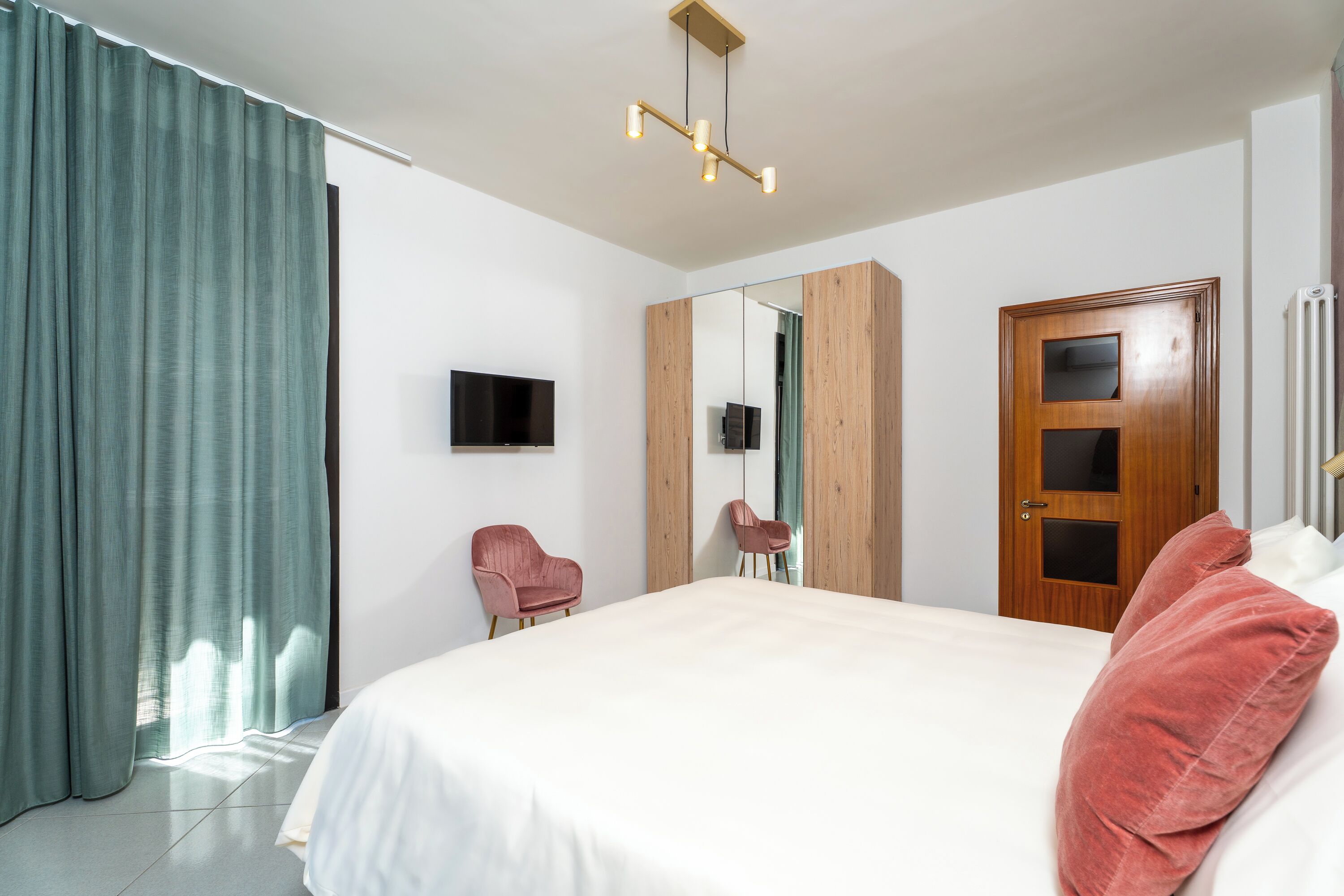Un dormitorio con cama, una silla, televisor, armario y puerta.