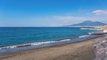 Une plage à l’eau d’un bleu limpide, avec un rivage rocheux et une montagne en arrière-plan.