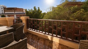 Una terrassa amb mobiliari de vimet, una barana de fusta i vista a edificis i arbres.