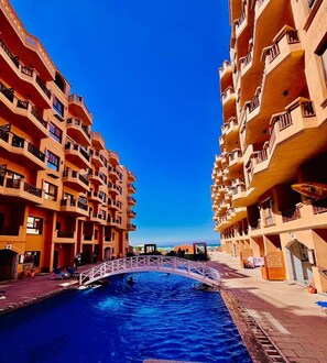 Ein mehrstöckiges Hotel mit Balkonen, einem Schwimmbad und einer Fußgängerbrücke.
