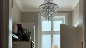 Ein Flur mit einer Chandelüster, einem Fenster mit Ausblick und einer Tür zu einem weiteren Raum.