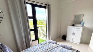 Ein Schlafzimmer mit einem Bett, Vorhängen, einem Fenster, einem weißen Schrank und einem Balkon.