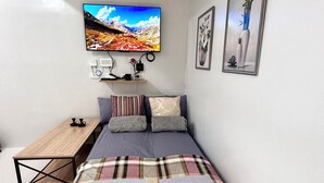 Ein Schlafzimmer mit einem Bett, einem an der Wand montierten Fernseher, einem Nachttisch und einem kleinen Regal.