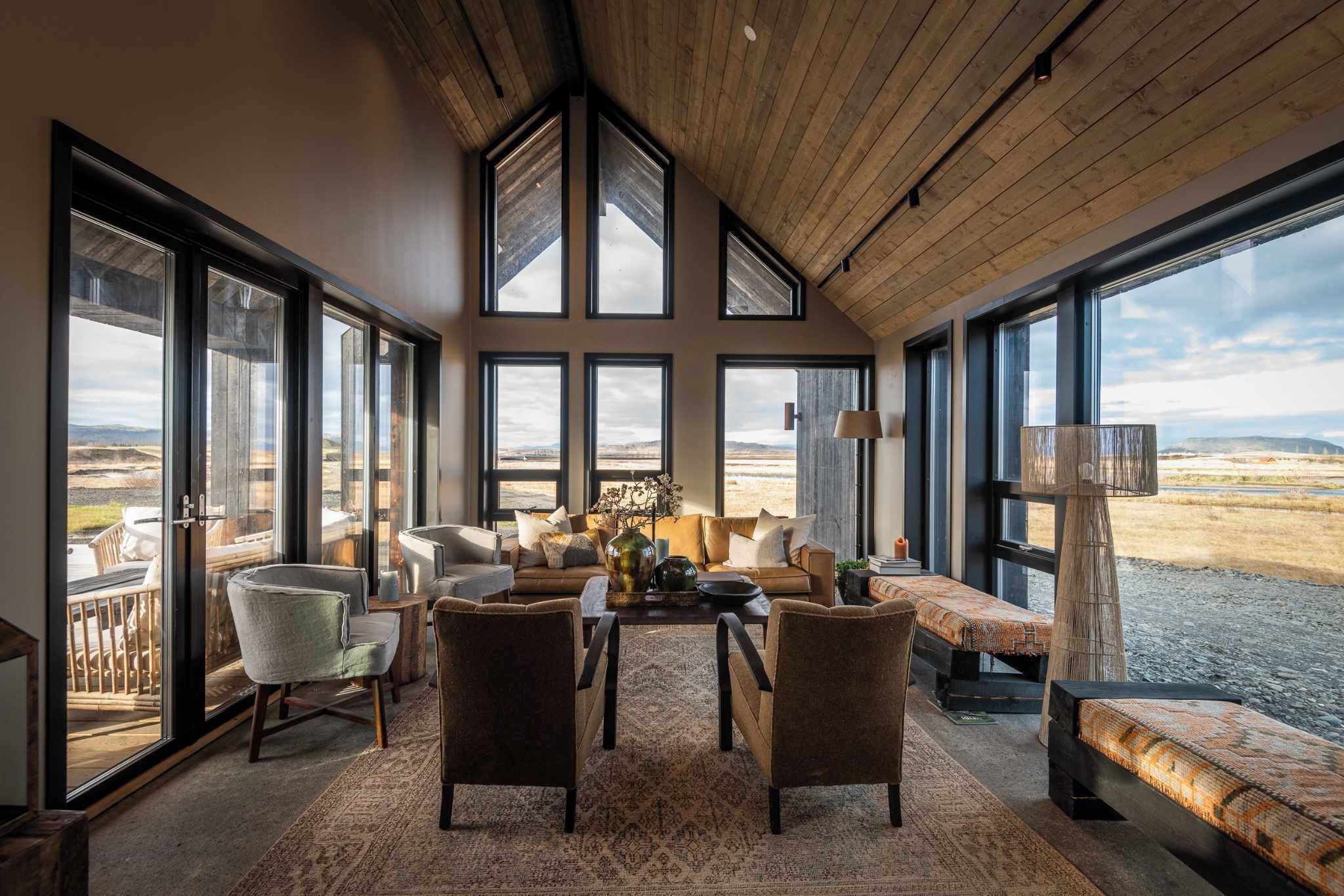 A spacious living area with large windows, a wooden ceiling, and a view of the landscape.