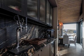A modern kitchen with a marble countertop, stainless steel appliances, and a dining area with a view. - Stuðlastrengur Luxury Private Villa (Skeiða- og Gnúpverjahreppur)
