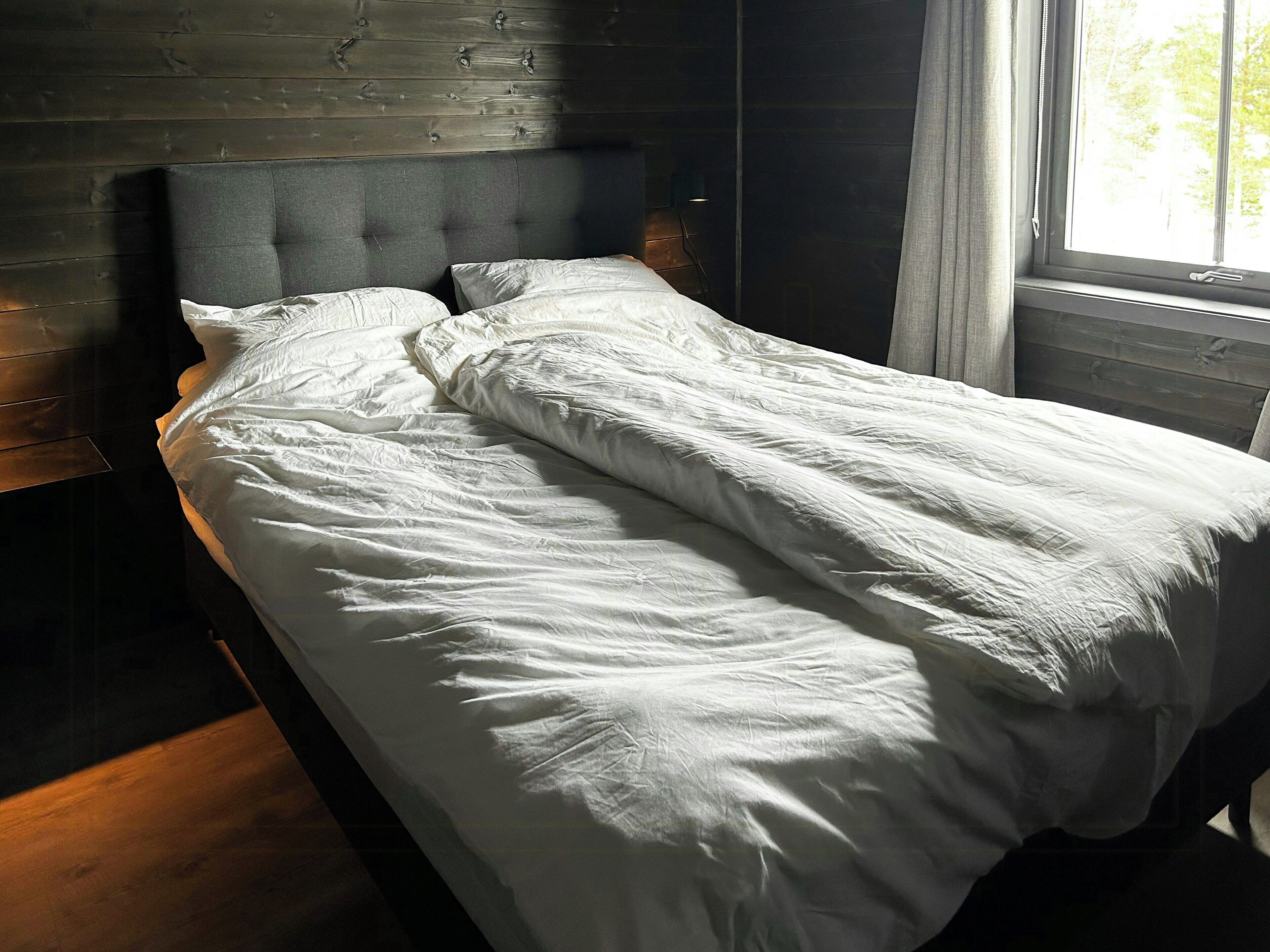 A bed with white bedding in a room with wooden walls and a window.