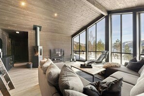 Ein modernes Wohnzimmer mit Kamin, großen Fenstern und einer gemütlichen Sitzecke.