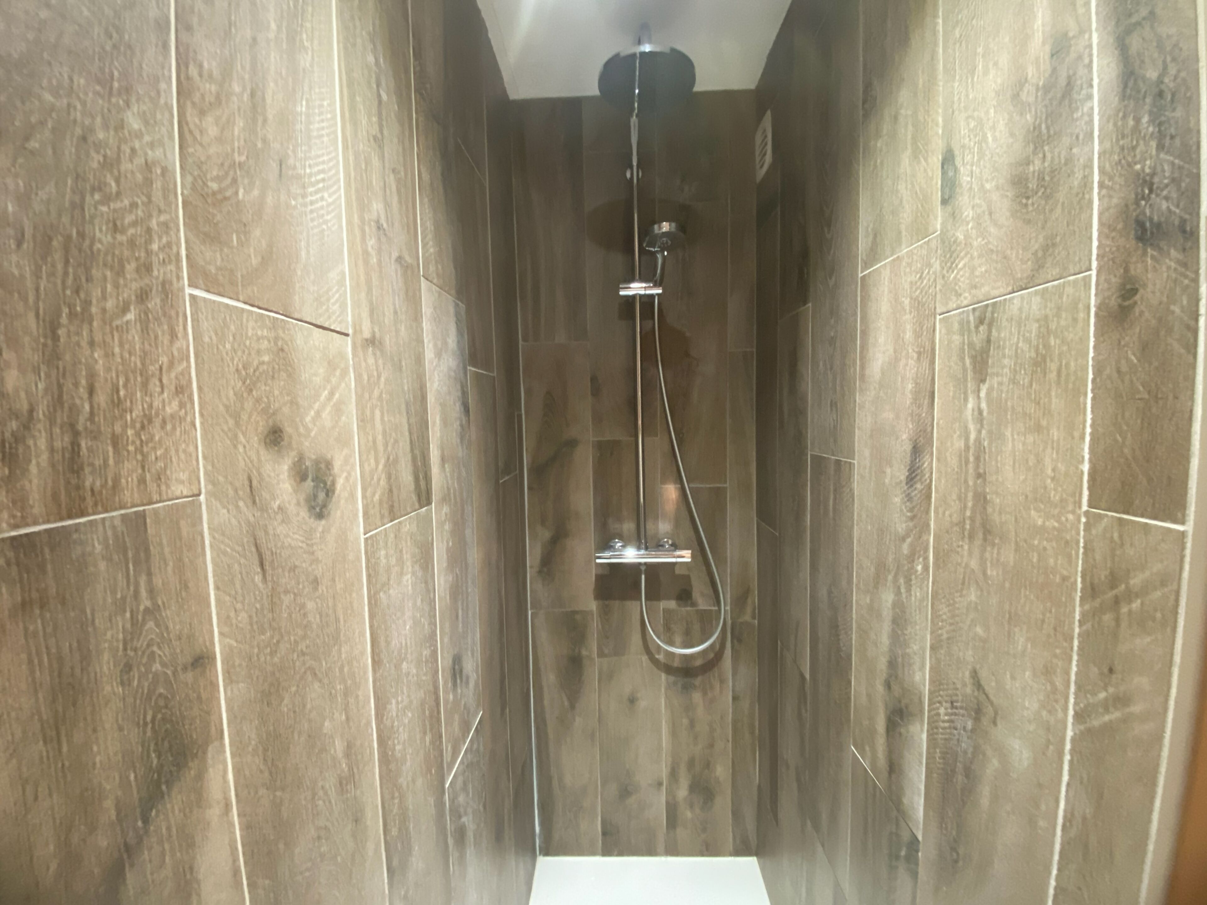 A shower with a handheld showerhead and a wall-mounted faucet.