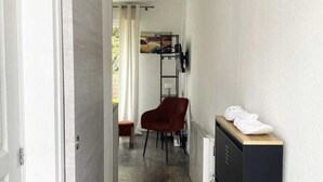 A narrow hallway with a door on the left, a red chair, a radiator, and a black cabinet with towels on top.