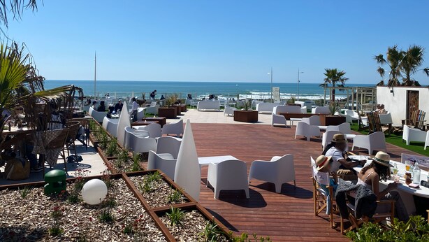 A terrace with white chairs and tables, overlooking the ocean.