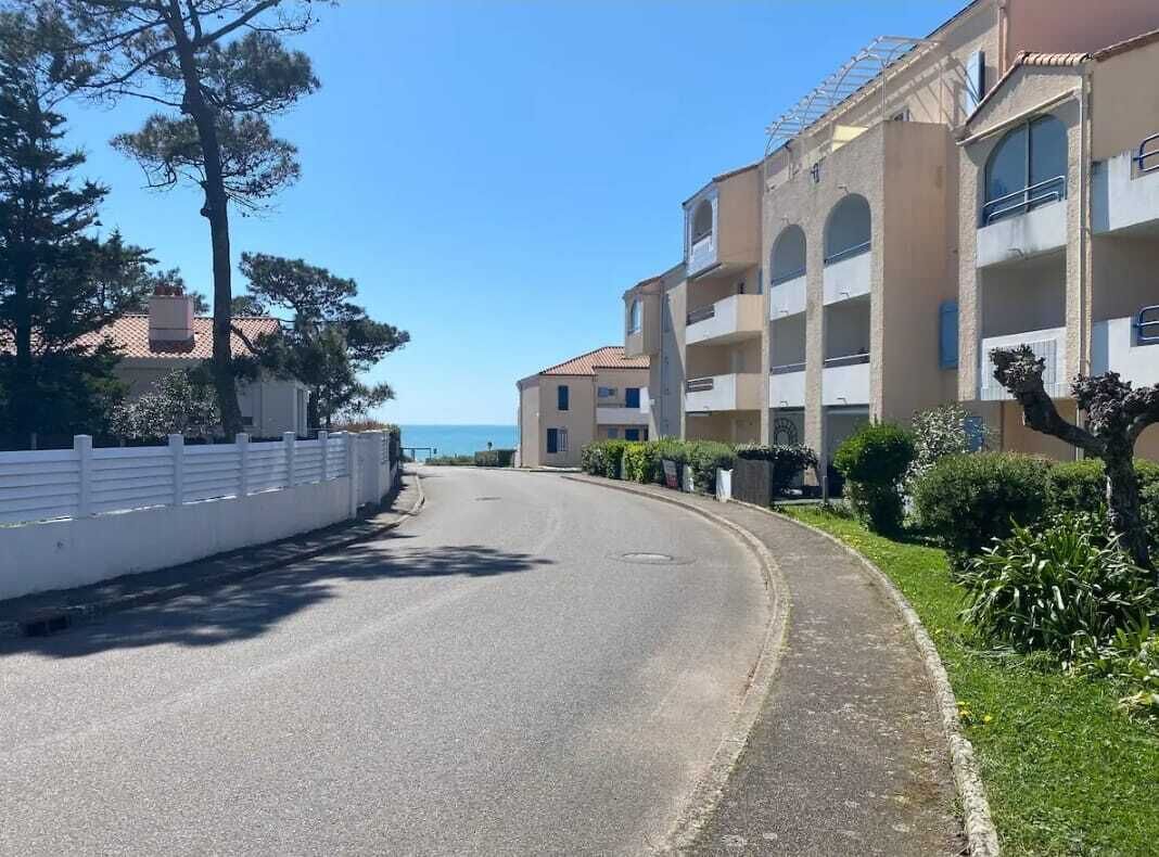 A curved road with a white fence on the left, a building with balconies on the right, and a clear sky.