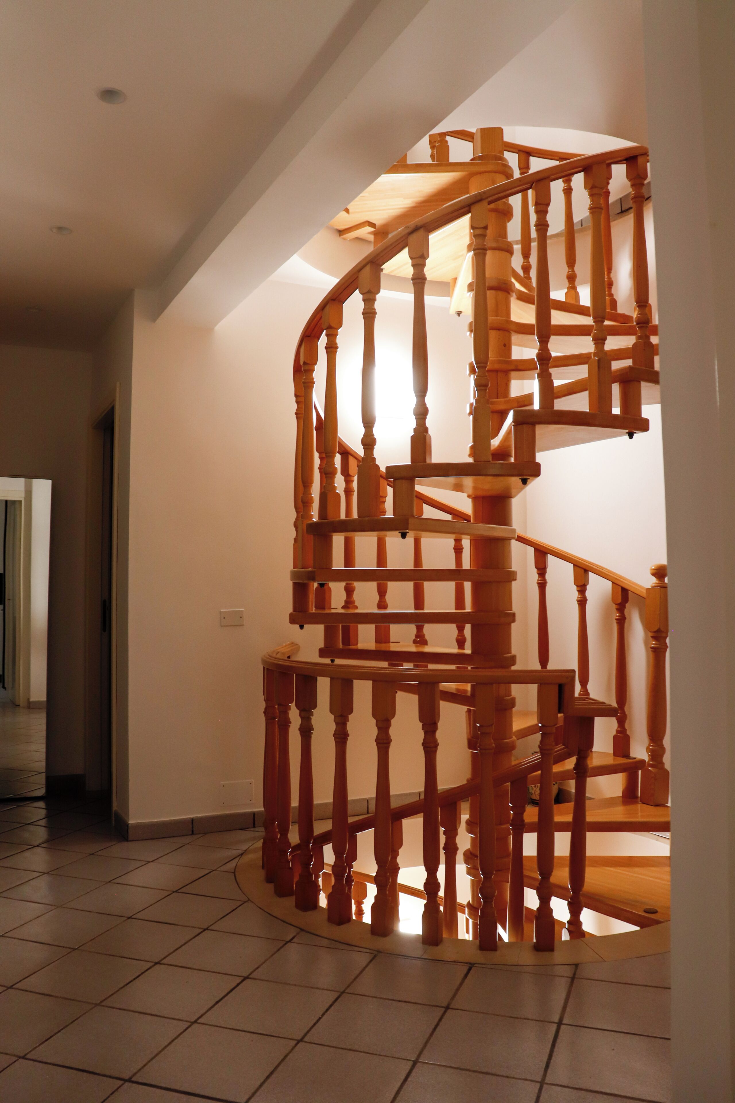 A spiral staircase with wooden balusters and a handrail, leading to an upper floor.