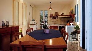 Uma área de refeições com mesa de madeira, cadeiras, toalha de mesa azul e um vaso com planta.