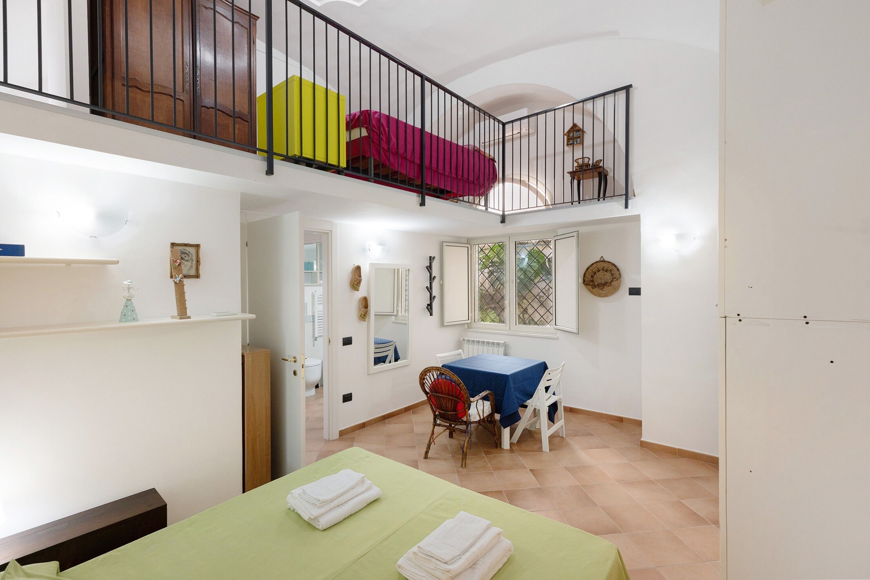 Un espace de vie compact comprenant un coin repas, un balcon avec une chaise rouge et jaune, et une petite table.