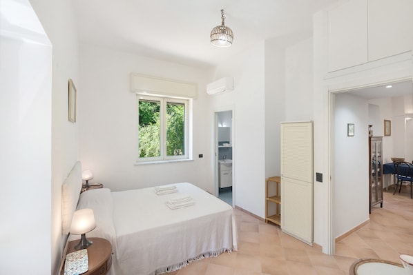 A bedroom with a bed, bedside lamps, a window, and a door leading to a bathroom.