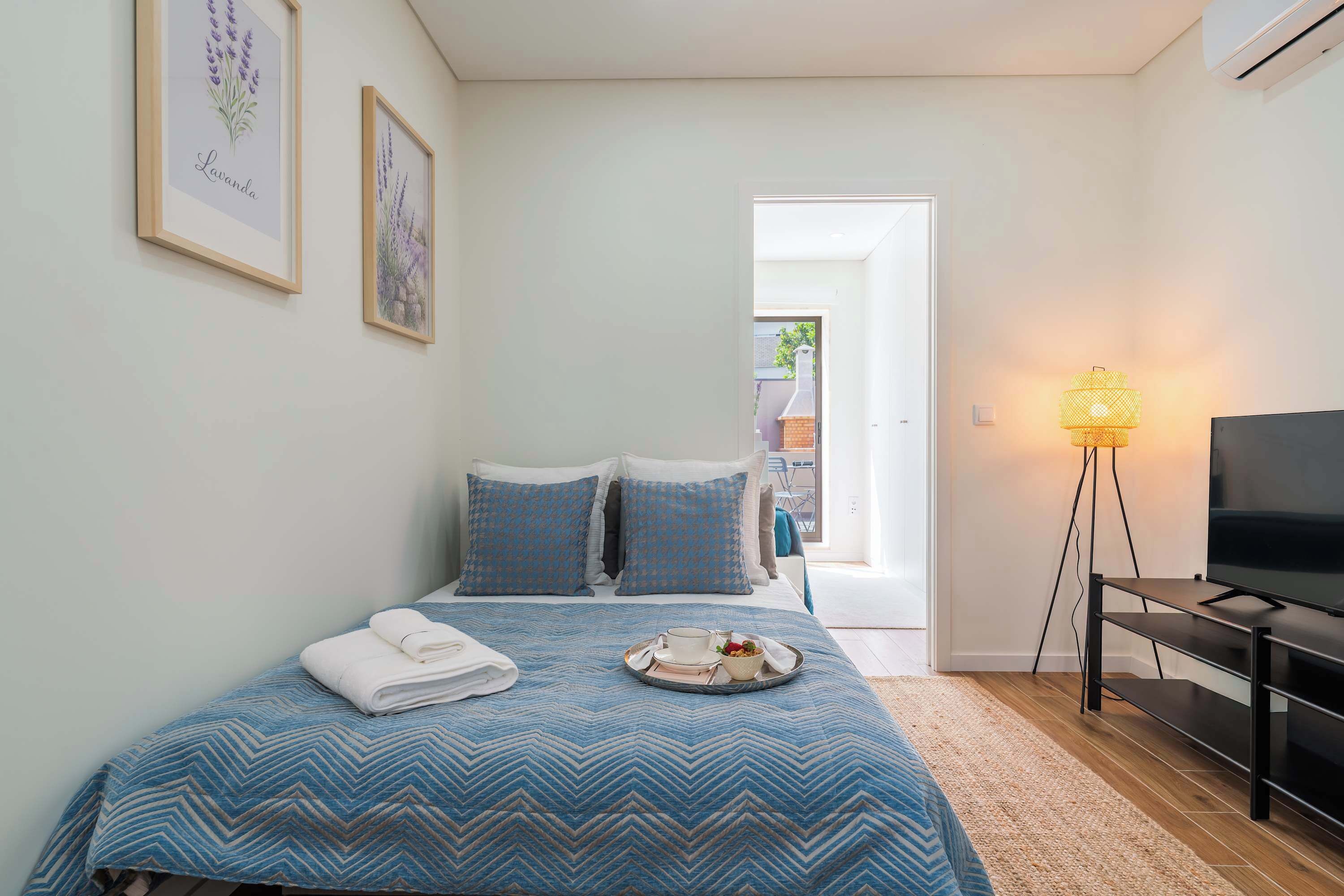 A bedroom with a bed, a tray with a cup and food, a TV, and a lamp.