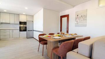 Una cocina moderna con electrodomésticos de acero inoxidable, un comedor con mesa de madera y sillas tapizadas en tono café, y un cuadro en la pared.