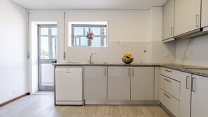 Ett modernt kök med vita skåp, en inbyggd diskmaskin, ett fönster med en vas med blommor och en dörr som leder ut.