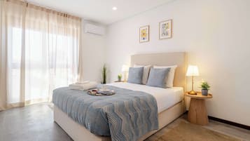 Un dormitorio con cama, lámparas de noche, una mesita con una planta y una ventana con cortinas.