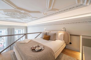 Ein Hotelzimmer mit Bett, Tablett mit Tasse und Buch, Nachttisch, Lampe und Balkonblick.
