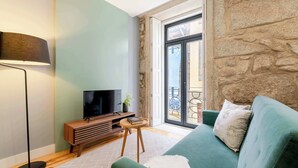Un soggiorno con un divano verde, una televisione su un mobile in legno, una lampada da terra e una parete in pietra.