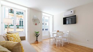 A modern living room with a sofa, a dining table with chairs, a TV mounted on the wall, and a potted plant. - Cozy Santa Catarina Studio by HostWise (Porto)