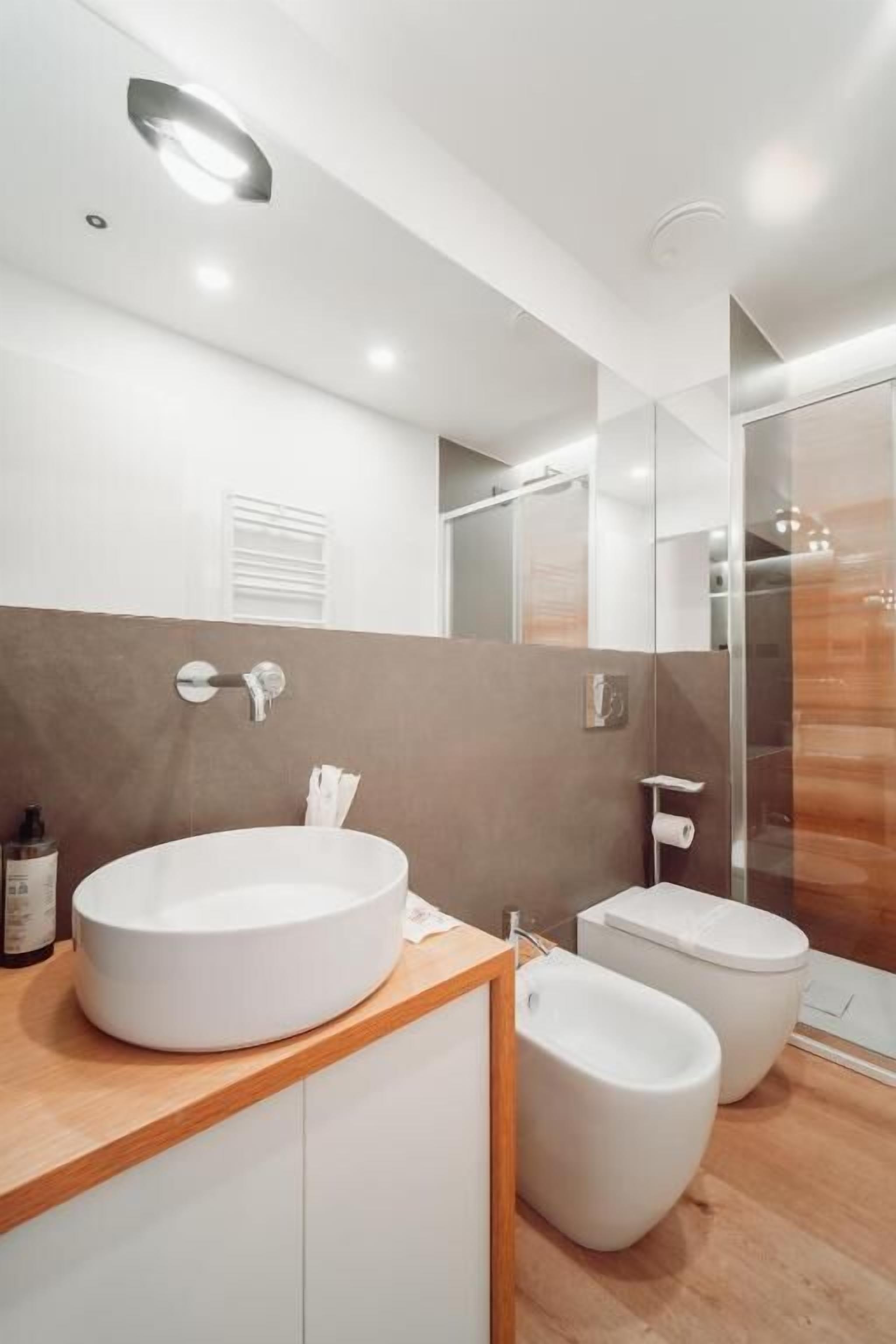 Un bagno moderno con un lavandino tondo, un bidet e un box doccia in vetro.