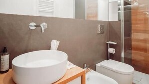 Een moderne badkamer met een rond wastafel, een hygiëneslot en een douchecabine van glas.