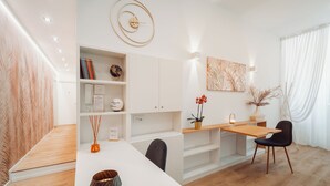 Een moderne eetruimte met een witte tafel, zwarte stoelen, een houten bureau en een klok aan de muur.