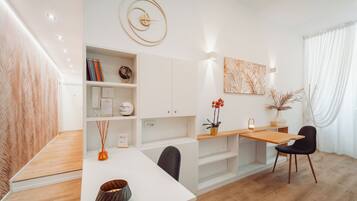 Een moderne eetruimte met een witte tafel, zwarte stoelen, een houten bureau en een klok aan de muur.
