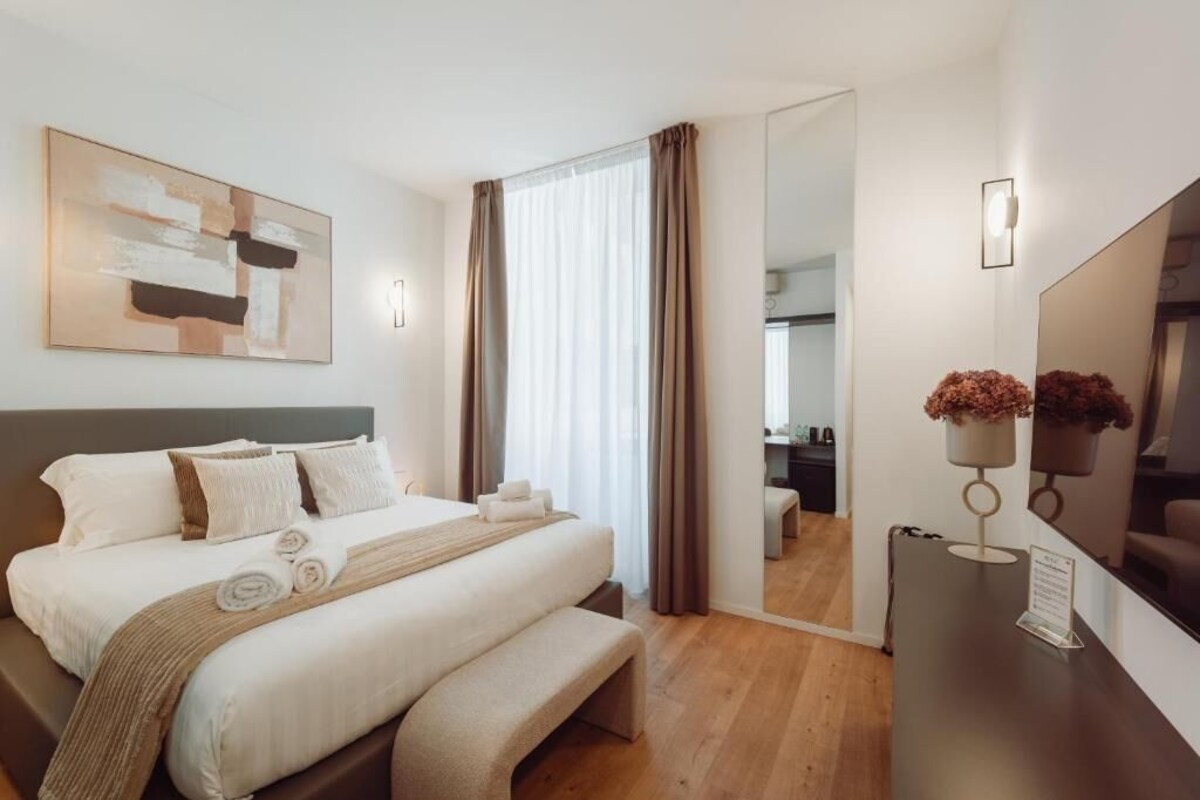 Habitación de hotel con cama, escritorio, silla, espejo y ventana con cortinas.