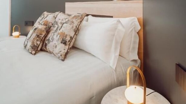 Een moderne slaapkamer met een bed, nachtkastje, lamp en decoratieve vaas.