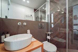 Un baño moderno con un lavamanos blanco grande, un inodoro y una cabina de ducha de vidrio.