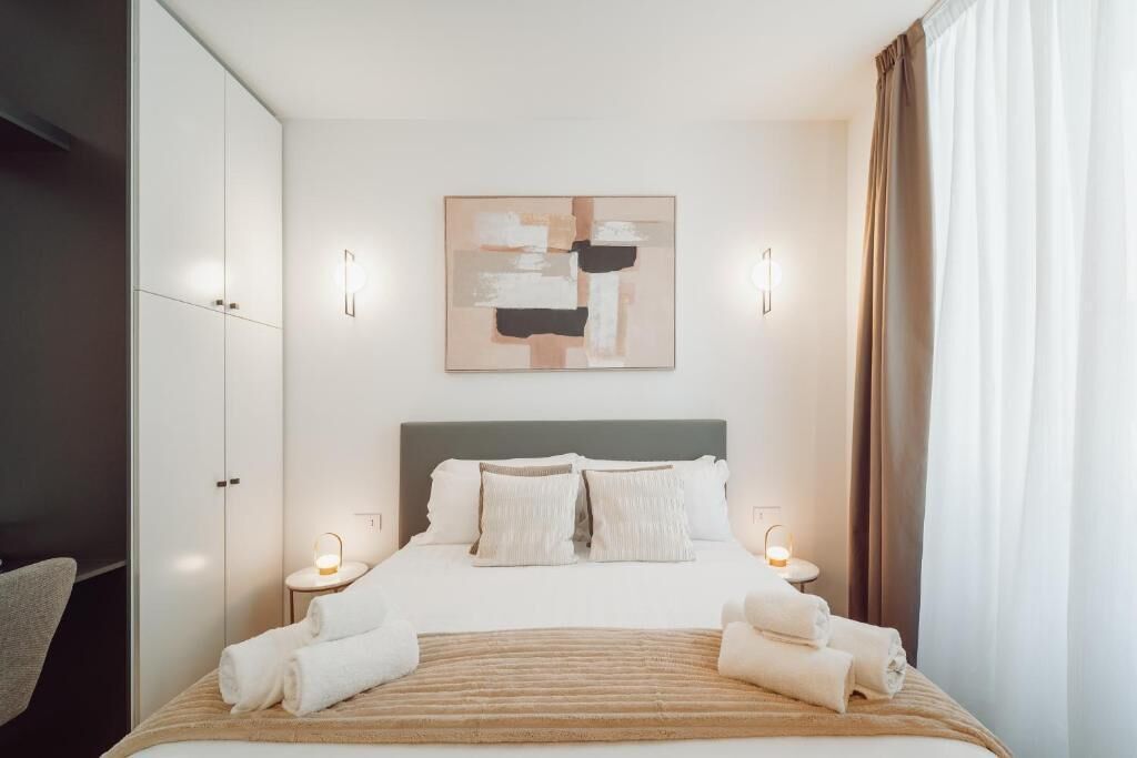 Ein Hotelzimmer mit Bett, Kopfteil, Wandbild, Nachttischlampen und Vorhang.