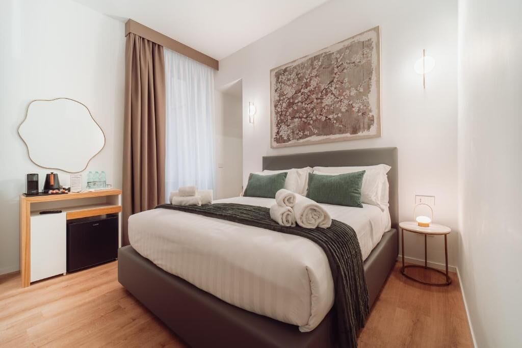 Een hotelkamer met een bed, een bureau, een stoel, een klein tafeltje en een wandlamp.