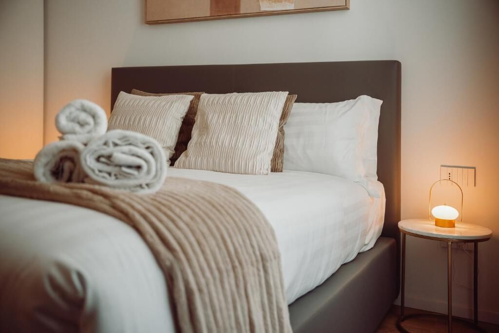 A neatly made bed with rolled towels, a bedside lamp, and a wall-mounted artwork.